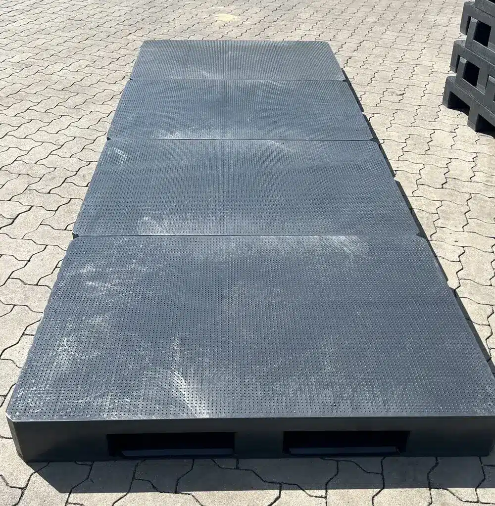 Vier anthrazitfarbene Kunststoffpaletten P18A mit genopptem Antirutsch-Deck in Reihe auf Pflasterboden