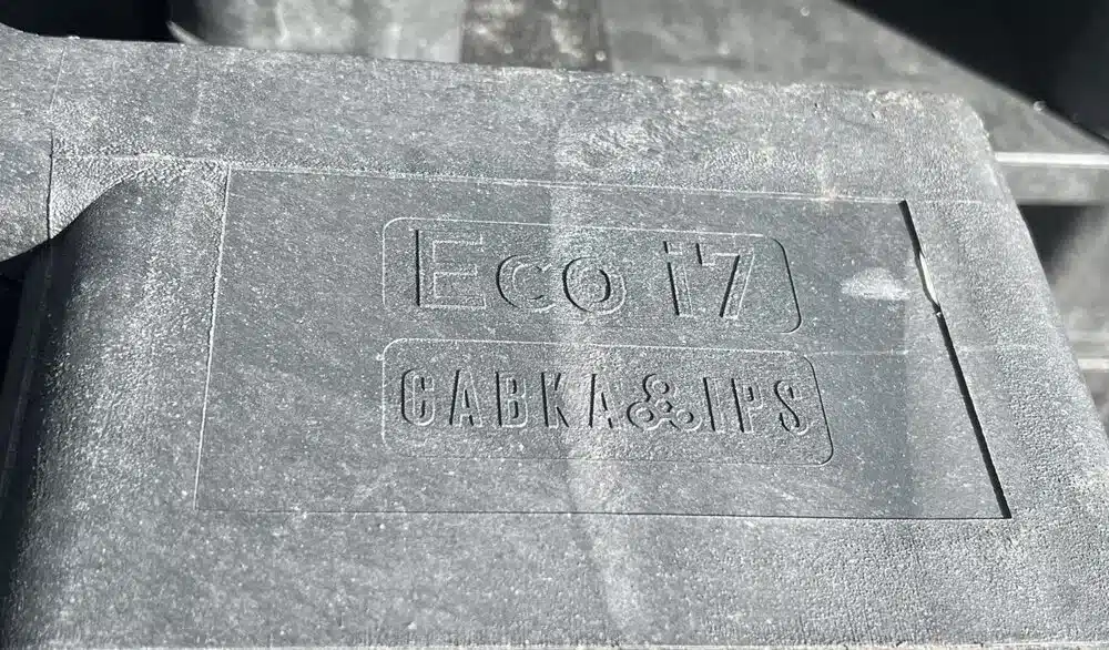Eingeprägter Schriftzug Eco i7 und Cabka IPS auf der Kufe einer dunklen Kunststoffpalette, Nahaufnahme