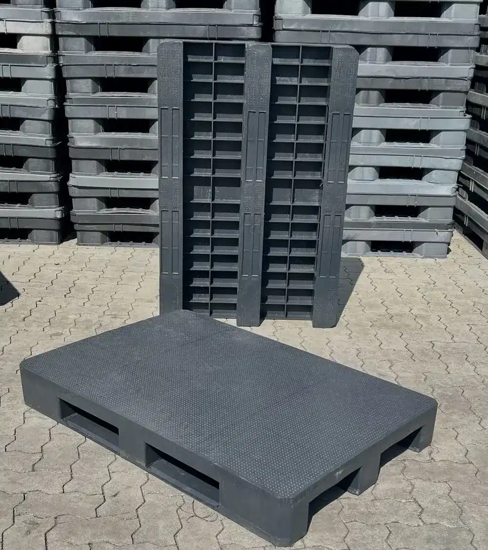 Massive Kunststoffpalette P18A liegend und hochkant mit Blick auf die Unterseite mit drei Kufen, Stapel dahinter
