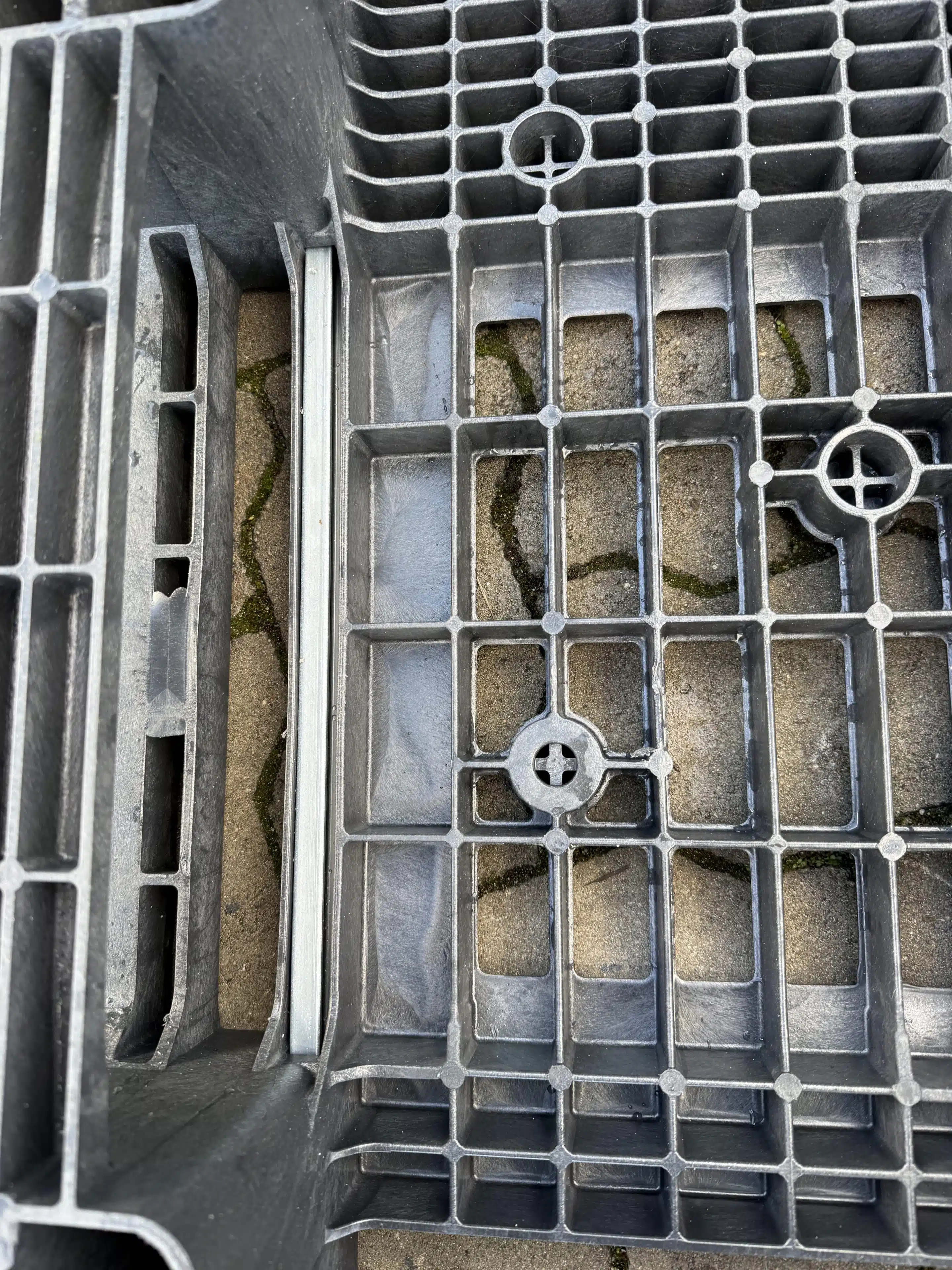 Nahaufnahme der Gitterstruktur einer schwarzen Kunststoffpalette auf gepflastertem Boden.