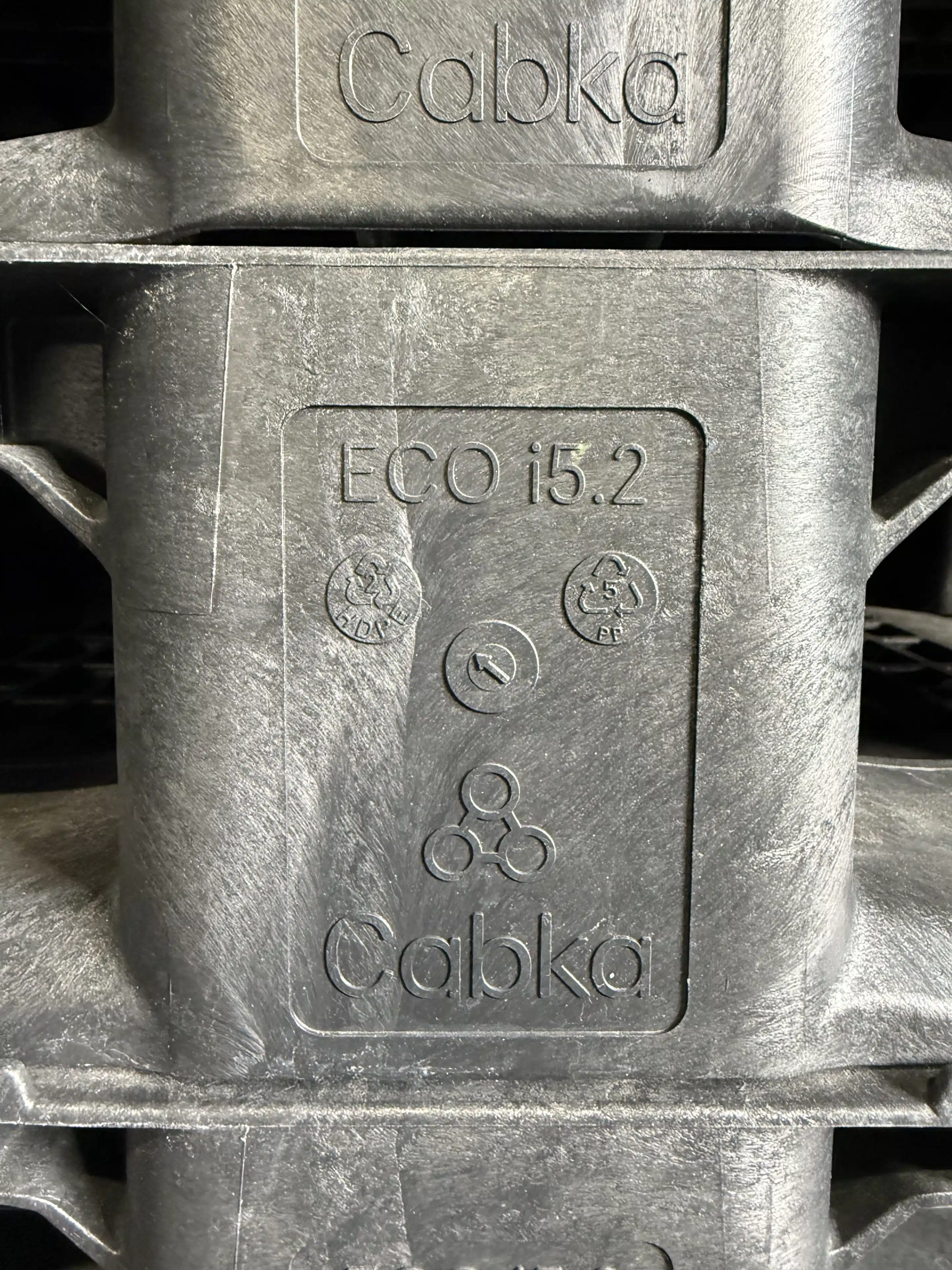 Nahaufnahme einer grauen Cabka ECO i5.2 Kunststoffpalette mit eingeprägtem Logo und Recyclingzeichen