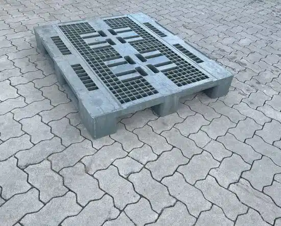 Graue Kunststoffpalette mit Gitterdeck steht auf gepflastertem Boden im Freien.