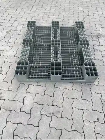 Graue Kunststoffpalette mit Gitterstruktur auf gepflastertem Boden im Freien.