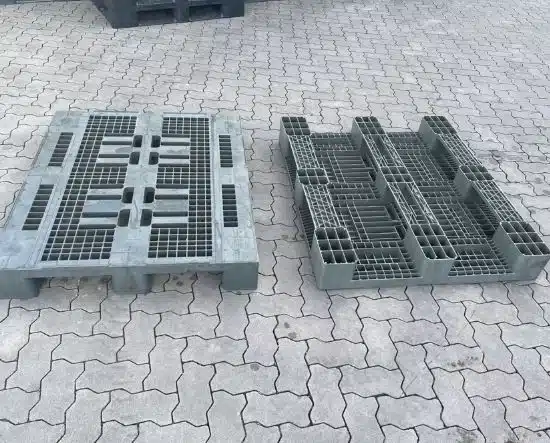 Zwei graue Kunststoffpaletten mit Gitterstruktur stehen auf gepflastertem Boden im Freien.